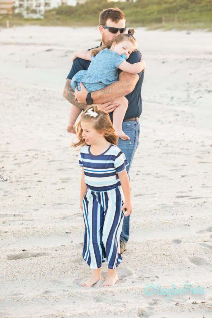 A man holding a baby and a girl walking on a beach. Vero Beach Photoshoot